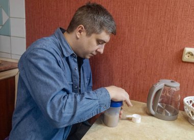 Adam mutfakta protein içeceği hazırlıyor. Tozu fitness, iyileşme ve kas sağlığı için karıştırıcıya dönüştürüyor..