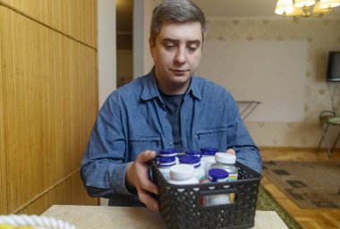 Adam evde beslenme takviyesi alıyor, şişeden ilaç dolduruyor ve suyla içiyor. Günlük vitaminler, sağlık hizmetleri ve sağlık rutini kavramı.