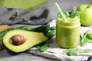 Avokado ıspanağı ve yeşil elma püresi sağlıklı ve ferahlatıcı tropikal bir içecek. Nane yaprakları ve dilimlenmiş avokado meyvesi, elma ve ıspanak yapraklı cam kavanozun yakın görüntüsü..