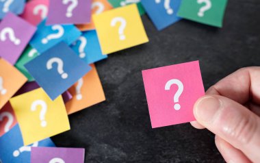 Müşteri sorunları kavramı, arka planda üzerinde soru işareti olan pembe bir kağıt tutan bir erkeğin yakın çekim görüntüsüyle ve daha pek çok renkli kağıtla..