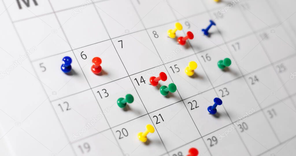 Business calendar page busy scheduling, time management, deadlines and events planning concept with many colorful push pins on a monthly paper calendar page.