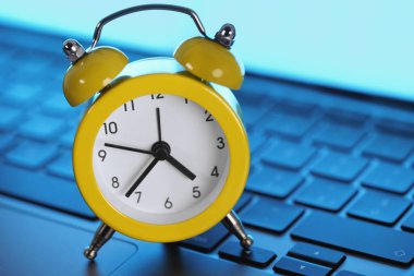 Yellow alarm clock on a laptop computer keyboard. Online business deadline, networking time management and daily business tasks planning concept.