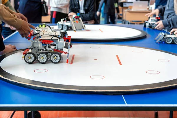 Bir okul çocuğu ekibi, kendi kendini yöneten LEGO robotları arasında yapılan ve yuvarlak bir robotik yarışma halkasındaki bir savaşı izliyor (LEGO Sumo)