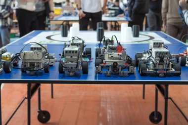 Öğrenci eli yarışmaya başlamak için programlanabilir bir DIY robotu hazırlıyor. Yarışmadan önce masaya dizilmiş özel yapım eğitici robotların çeşitliliği.