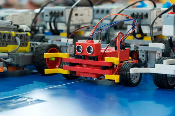 Bir STEM robotik turnuvası sırasında mavi bir yarışma arenasında duran ultrasonik sensörlü kırmızı bir robot da dahil olmak üzere kişiselleştirilmiş eğitim robotlarının yakın çekim görüntüleri.