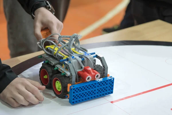 Bir STEM robotik yarışması sırasında LEGO marka özel bir robotu yarış minderinin üstünde ön pullukla ayarlayan bir öğrencinin yakın çekimi