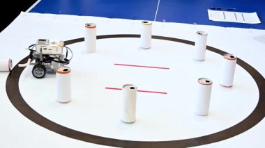 Robot, robot oyunu oynuyor. Bir STEM robotik yarışması sırasında silindirik hedefleri ringin dışına itmek için dairesel beyaz bir arenada gezinen programlanabilir bir eğitim robotu.