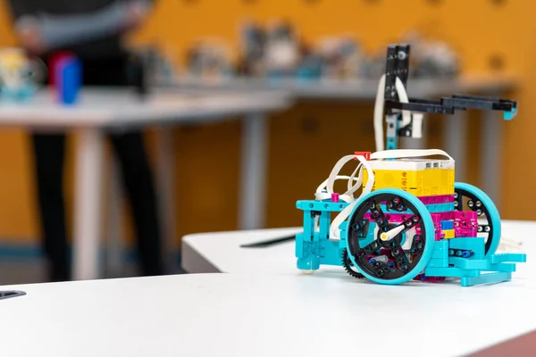 Bulanık bir sınıf arka planına sahip beyaz bir masada renkli programlanabilir bir robotun yakın çekimi. Eğitimsel bir inşaat setinin detaylarını vurgulayan yüksek kalite çekim.