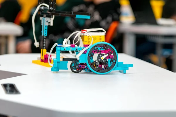 Mavi ve sarı bileşenleri olan özel yapım, modüler programlanabilir bir robot dikey kırmızı plastik bir engelin yanında bir yarışma alanı minderinin üzerine yerleştiriliyor. Alan çizgi-takip navigasyonu için eğri siyah çizgiler içerir.