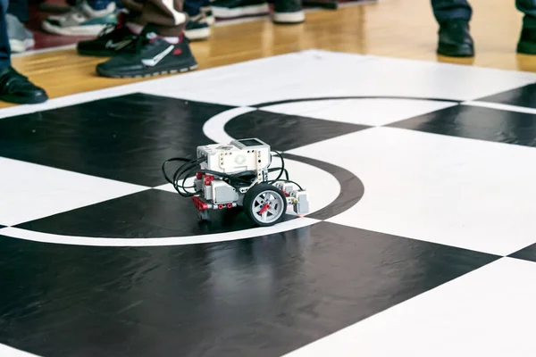 Büyük tekerlekleri, vitesleri, renkli kabloları ve parlak siyah-beyaz döşemedeki sensörleri olan parlak kırmızı LEGO robotu el ile yönlendirmek veya ayarlamak. Robot, kapalı bir robotik yarışmasında kavisli bir siyah çizgi çiziyor.