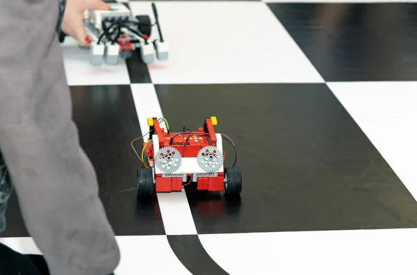 Robot, kapalı bir robotik yarışmasında veya eğitim etkinliğinde, görünür motorlar ve LEGO Teknolojik elementleriyle mühendislik, programlama ve çocukların STEM aktivitelerini gösteren eğri bir siyah çizgi yolunda ilerliyor..