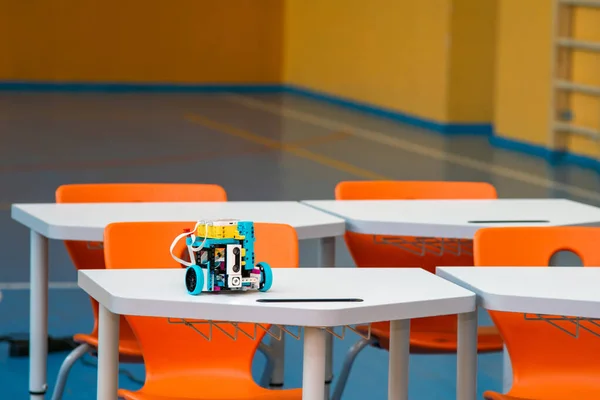 Boş bir modern sınıfta ya da okul salonunda beyaz bir masada oturan programlanabilir küçük bir DIY robotu. Çocukların robot bilimi, BTMM okul ekipmanları ve okul sonrası teknoloji programları kavramı.