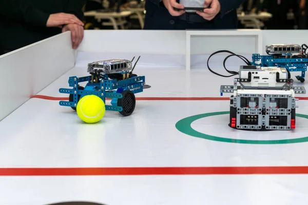 Kırmızı çizgili ve yeşil merkezli beyaz oyun alanında küçük, özel yapım robotları kontrol eden bir grup genç. Çevre. Robo futbol tarafından kontrol ediliyor.