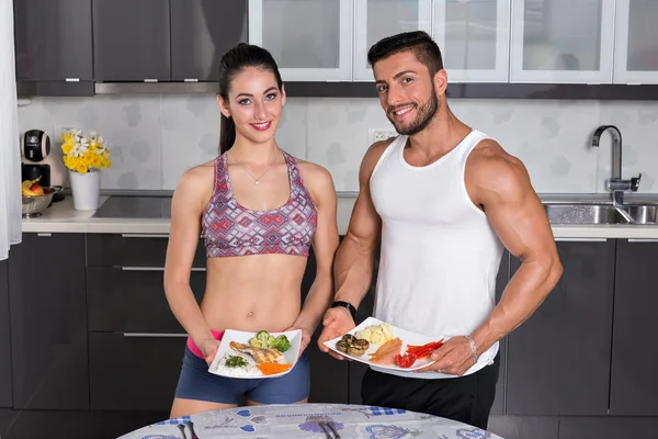 Casal ajuste na cozinha, segurando pratos de comida — Fotografia de Stock