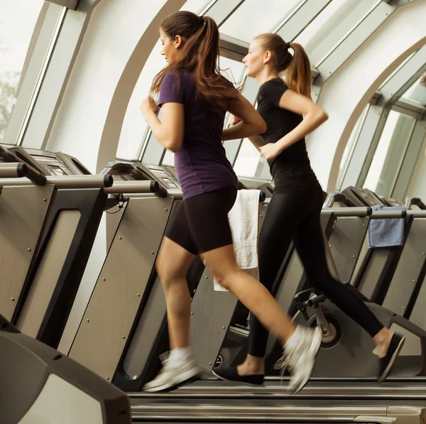 Gym skott, två unga kvinnor kör på maskiner, löpband — Stockfoto