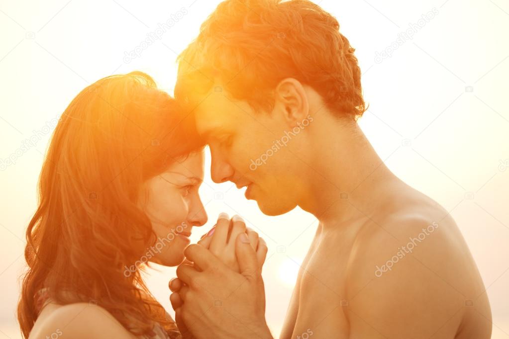 A loving young couple hugging and kissing on the beach at sunset
