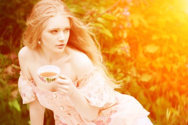 Beautiful woman with flowering tree drinking tea in sunset in sp