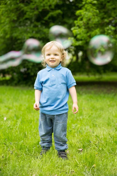 Lindo bebé rizado con burbujas de jabón. niños jugando, corriendo A —  Fotos de Stock
