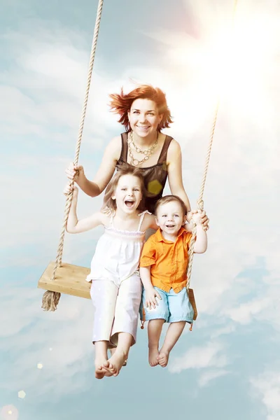 Diversión familiar. Mamá, hija, hijo riendo en un columpio contra el s — Foto de Stock