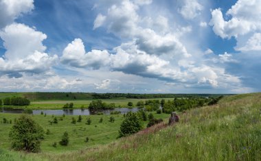 Otların arasında bir tepe, bend, nehir ve h üzerinde mavi bulutlar