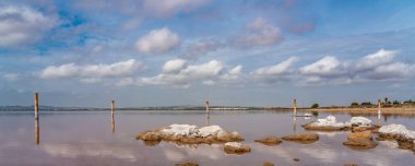 Rocks in a pink salt lake Laguna Rosa, Torrevieja, reflection on water from clouds, panorama