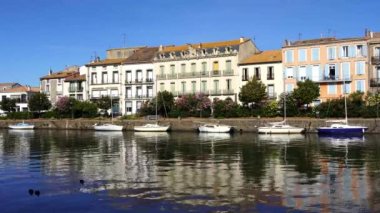 Herault nehri kıyısındaki eski binalarla Agde Center, yazın nehir kıyısındaki teknelerle şehrin sokak manzarası.