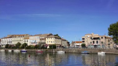 Herault nehri kıyısındaki eski binalarla Agde Center, yazın nehir kıyısındaki teknelerle şehrin sokak manzarası.