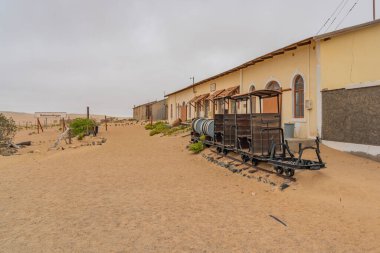 KOLMANSKOP, NAMIBIA - 8-2021: Alman Kolmanskop - Kolmannskuppe Hayalet Kasabası Namibya 'da terk edilmiş binalar ve bir trenden alınan bir vagon