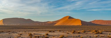 Sabah vakti Sossusvlei 'deki Namib Çölü' nün kumullarından gelen manzara, arka plan mavi gökyüzü güzel bulutlarla, Namib Naukluft Rand, Namibya.