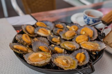 tasty seafood - grilled limpets served on black plate. Lapas grelhadas. Azores traditional dish and a typical snack of the Canary Islands. Grilled Limpets in Azores Islands. clipart
