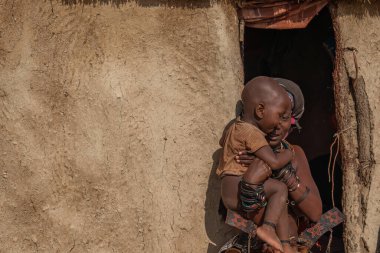 KORIXAS. NAMIBIA, 13 OCAK. 2020: Korixas, Namibya yakınlarındaki Himba köyündeki bir kulübede oturan Himba 'lı bir çocuk ve annesinin yan görüntüsü
