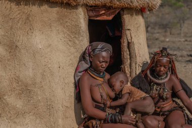KORIXAS. NAMIBIA, 13 OCAK. 2020: Korixas, Panorama yakınlarındaki Himba köyünde bir kulübenin önünde oturan iki üzgün Himba kabilesi kadını.