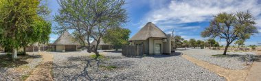 OKAUKUEJO, NAMIBIA - JANUARY 14, 2020 : Okaukuejo resort with thatched roof houses and pool in Etosha National Park, panorama clipart