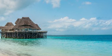 ZANZIBAR, TANZANIA - 12 Şubat 2020: Suyun üzerinde sazdan çatısı olan Zanzibar adasının tropikal beyaz plajı