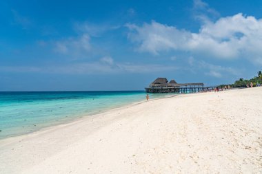ZANZIBAR, TANZANIA - 12 Şubat 2020: Zanzibar adasında suyun üzerinde sazdan bir çatısı olan tropikal beyaz plajdaki insanlar.