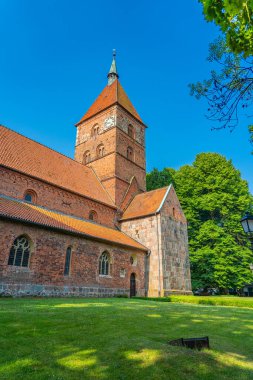 Wildeshausen 'deki İskender Kilisesi' nin arka planında yeşil ağaçlar ve mavi gökyüzü var.
