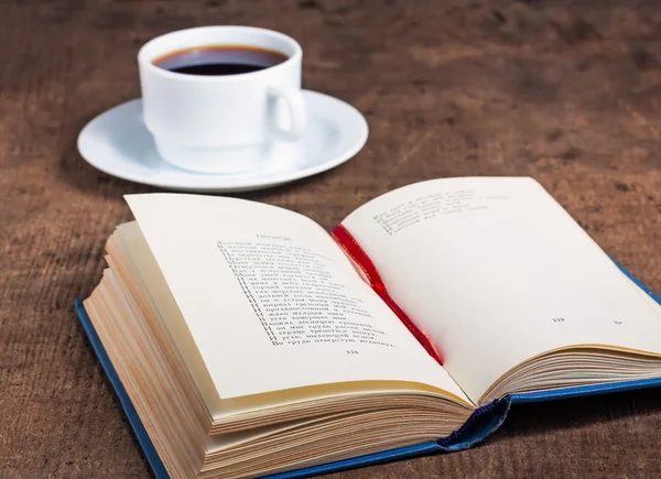 Libro aperto e una tazza di caffè su una superficie di legno — Foto Stock