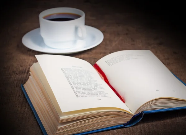 Otevřená kniha s šálkem kávy na dřevěný stůl — Stock fotografie