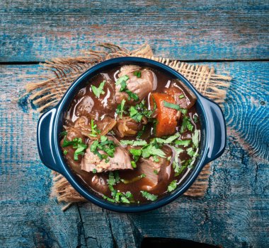 Meat stew with vegetables and herbs on old wooden table clipart