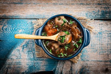 Meat stew with vegetables and herbs on old wooden table clipart