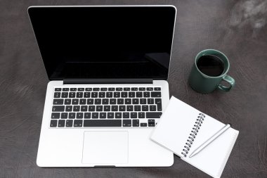 Bir defter ve dumanı tüten kahve ile masa üstünde laptop