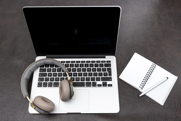 Laptop em uma mesa com fones de ouvido e um bloco de notas — Fotografia de Stock