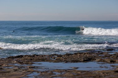 Dalgalar uzaktaki sörfçülerle çarpışıyor