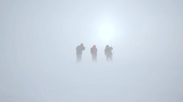 Tre personer i en snöstorm på bakgrunden av solen — Stockvideo