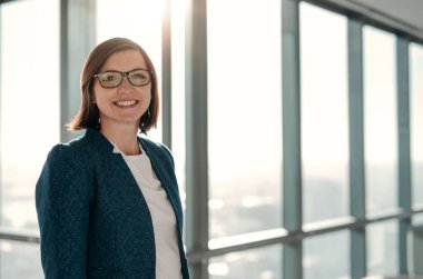 Şehre tepeden bakan bir ofis binasının penceresinin önünde duran çekici bir iş kadınının portresi.