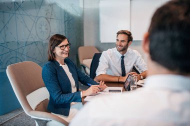 Bir grup başarılı iş adamı ofis yönetim kurulunda masa başında çalışırken birlikte konuşuyorlar.