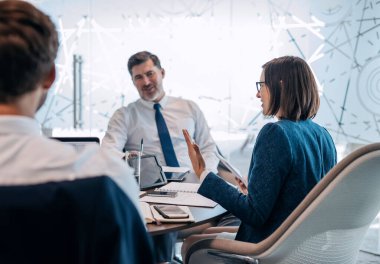 Bir grup başarılı iş adamı ofis yönetim kurulunda masa başında çalışırken birlikte konuşuyorlar.