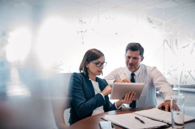 Modern bir ofiste masa başında çalışırken dijital tablet kullanan kendine güvenen iki iş adamı.