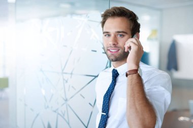 Parlak, modern bir iş ofisinde cep telefonunu kullanırken kameraya bakan genç bir profesyonelin portresi.