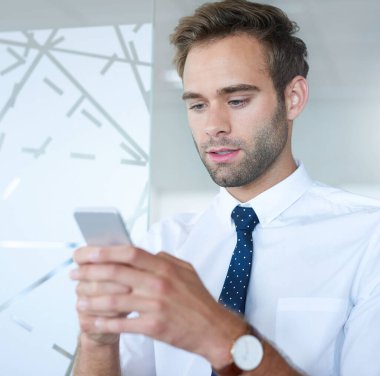 Modern bir iş yerindeki yakışıklı genç işletmeci bir mesaj yazarken cep telefonunun ekranına bakıyor.